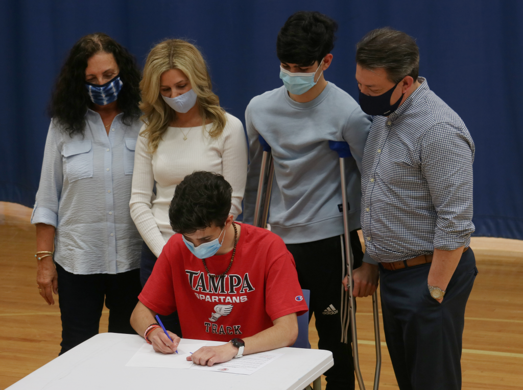 student athlete signing letter with family behind him watching him do it