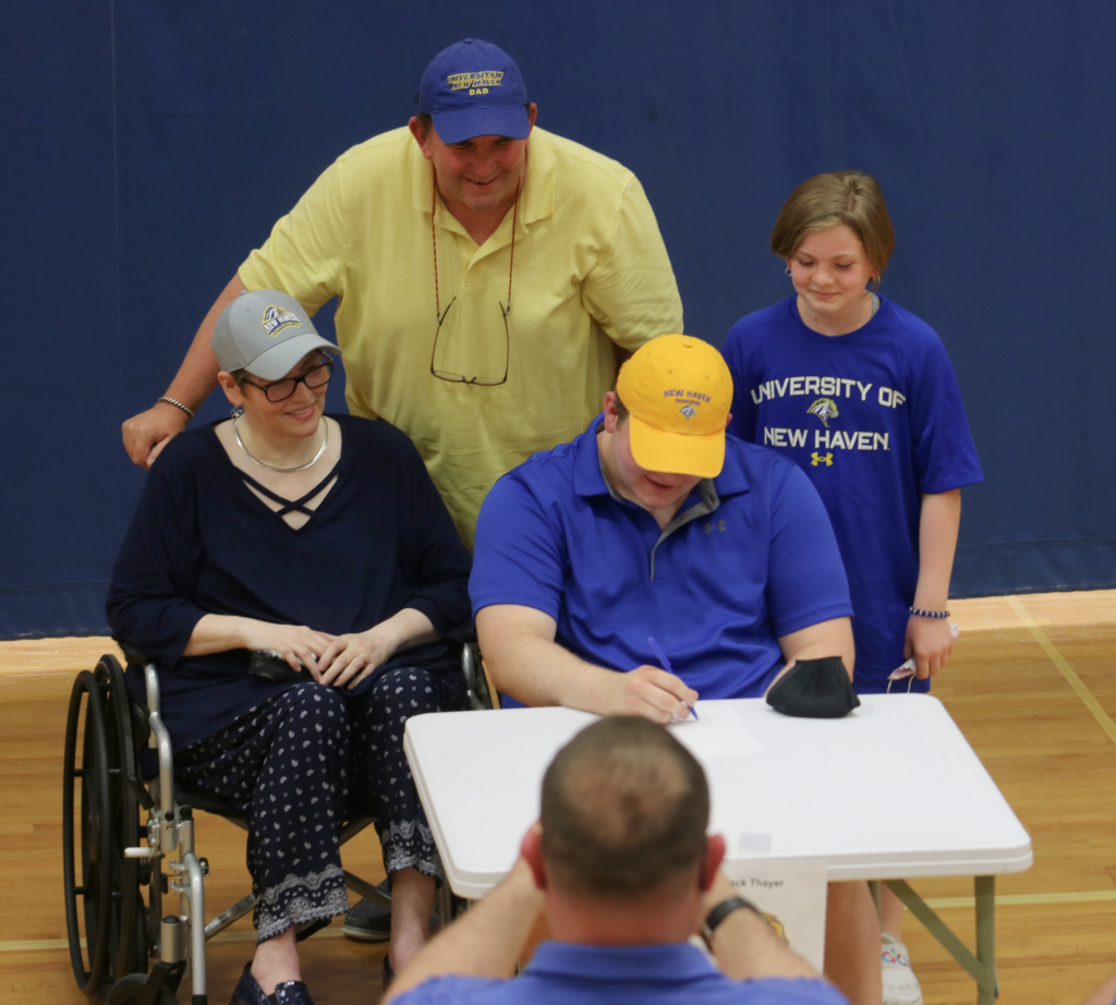 student athlete signing commitment letter with mom, dad, and sister looking proudly at him