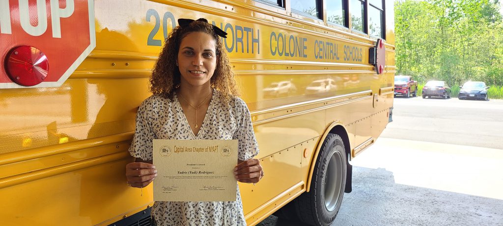 woman standing behind bus holding a certificate
