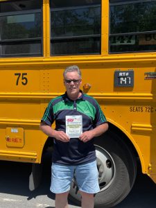 man standing in front of a bus holding a plaque