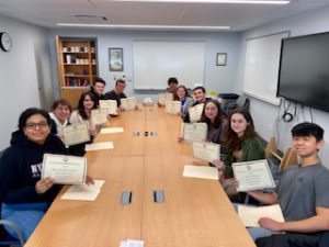 SHS music students seated at conference table with award certificates.
