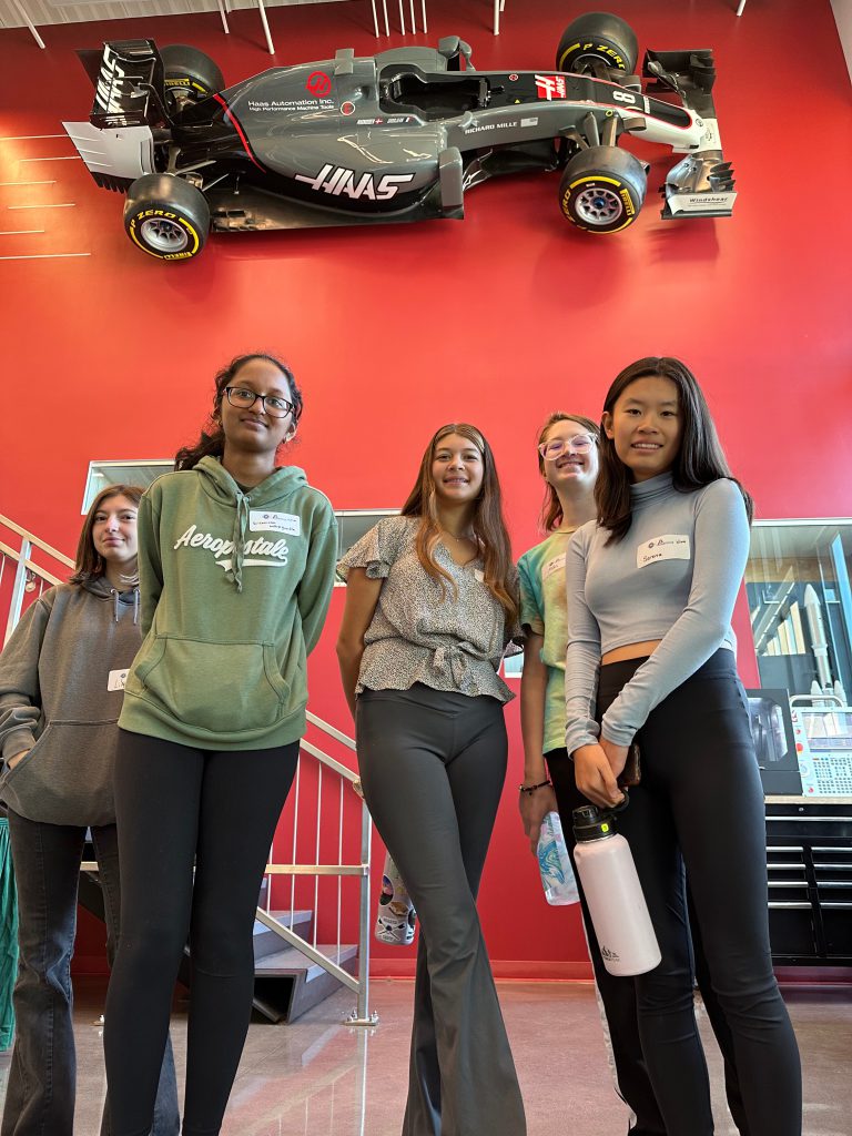 A picture looking up at the five Shaker students with a race car mounted on the wall behind them.