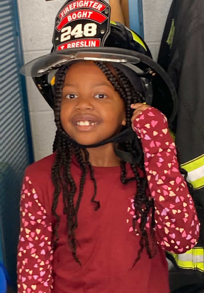 An image of a student smiling as she wears a fire fighter's helmet.