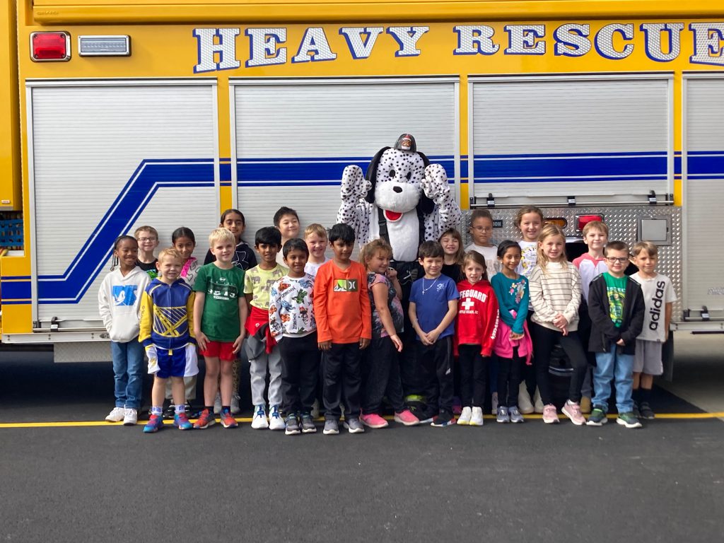 An image of a class of students posing with the fire dog mascot in front of a fire truck.