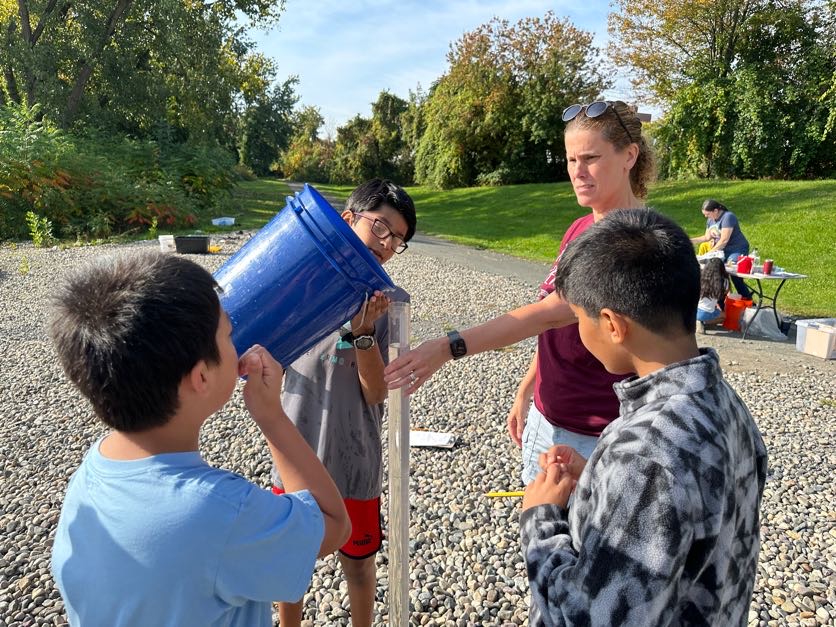 An image of students filling a large tube with water from the Hudson River.