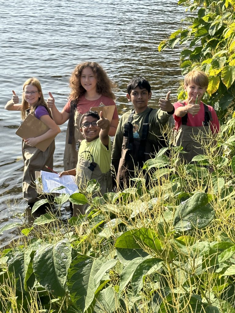 An image of five elementary school students giving thumbs up while standing in the Hudson River.
