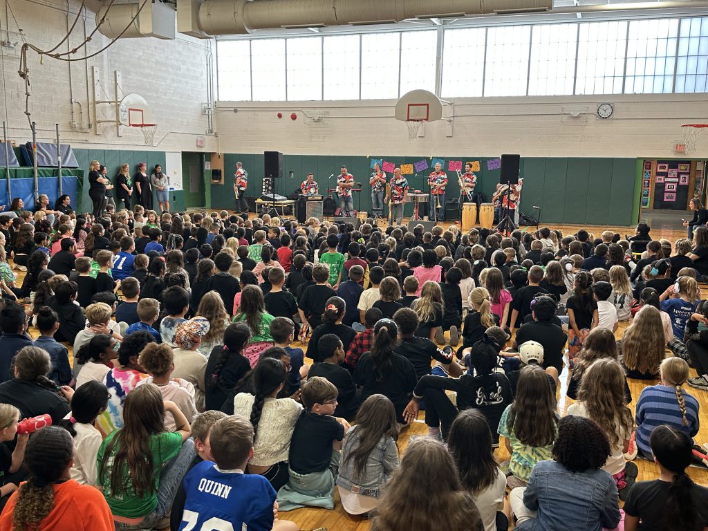 An image of a gymnasium full of students watching Alex Torres & His Latin Orchestra.