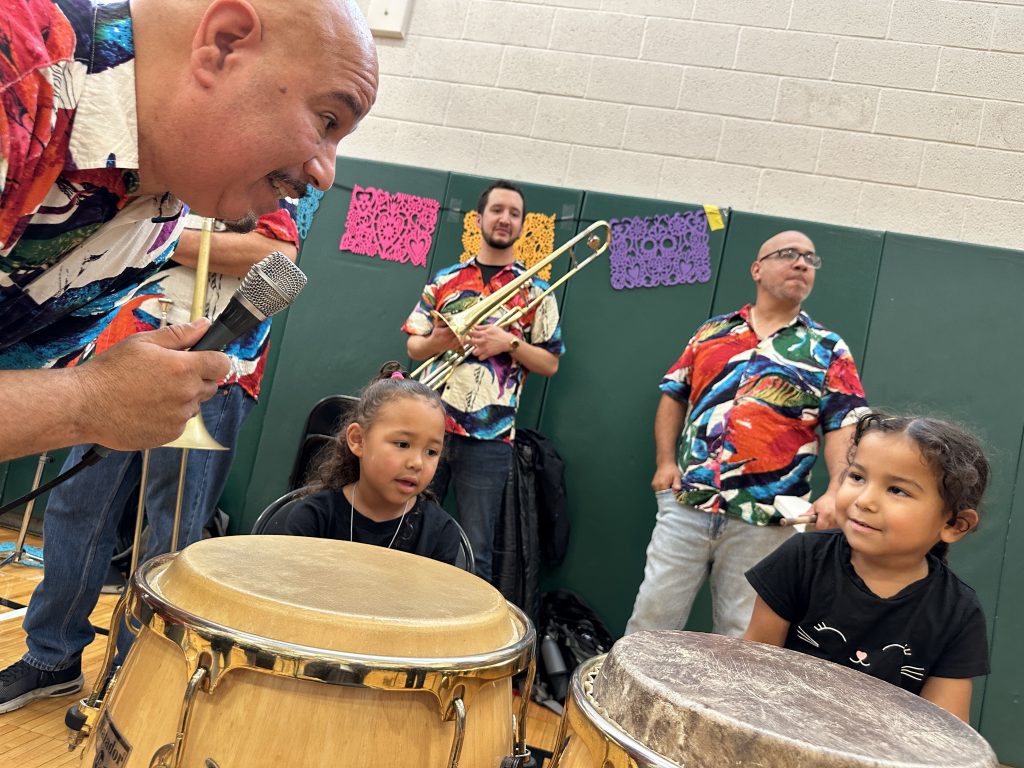 An image of two students help Alex on the conga drums.