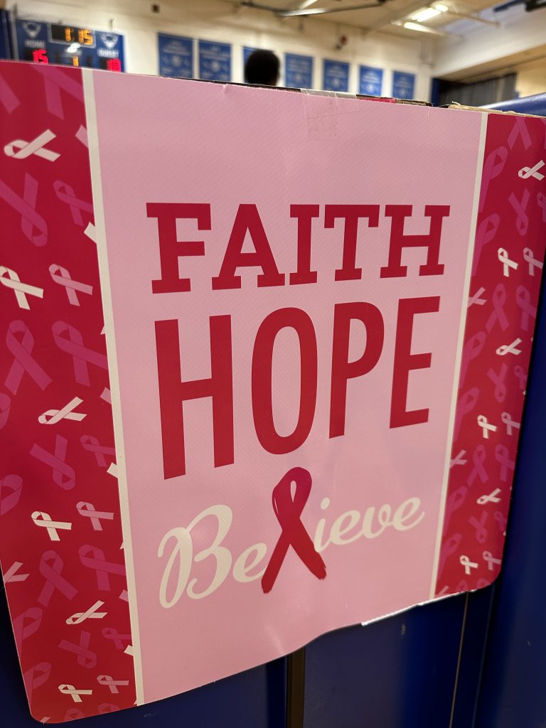 An image of a sign that says "Faith, Hope, Believe" with a pink breast cancer ribbon.