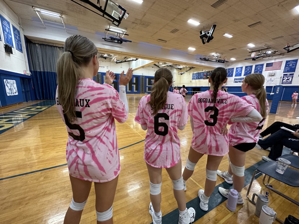 An image of the visiting Colonie volleyball players looking on during the game, also wearing pink.