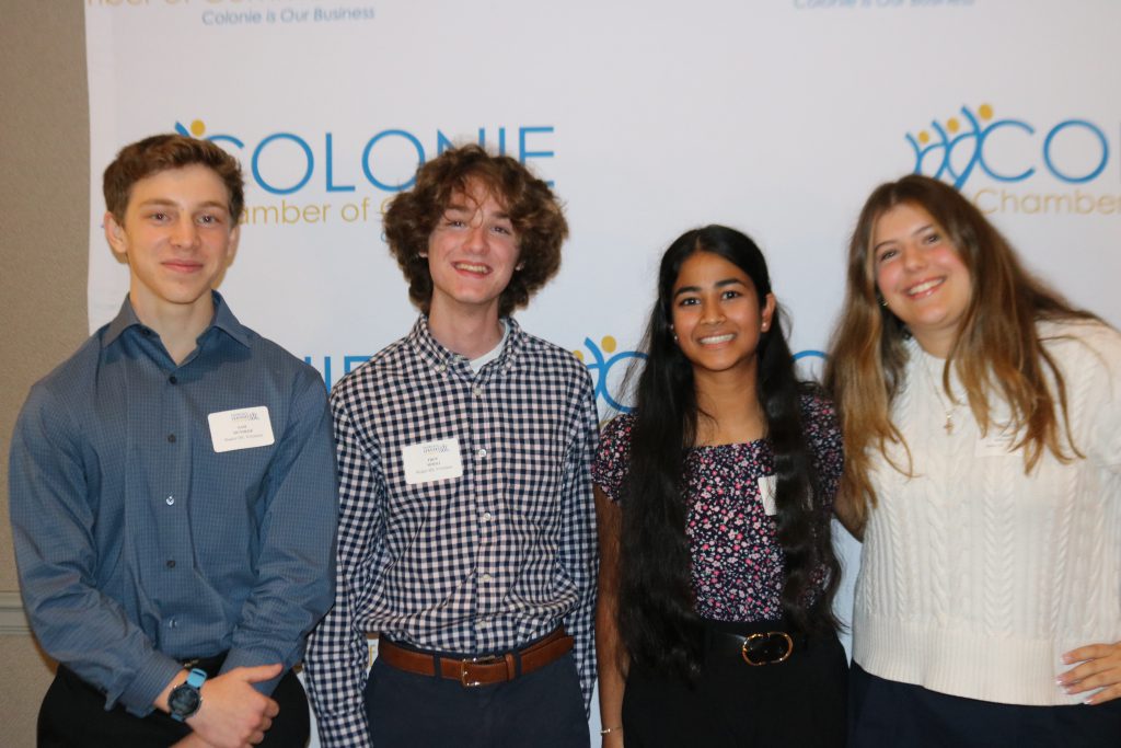 An image of four students posing in front of a banner at the Emerging Leaders Summit.