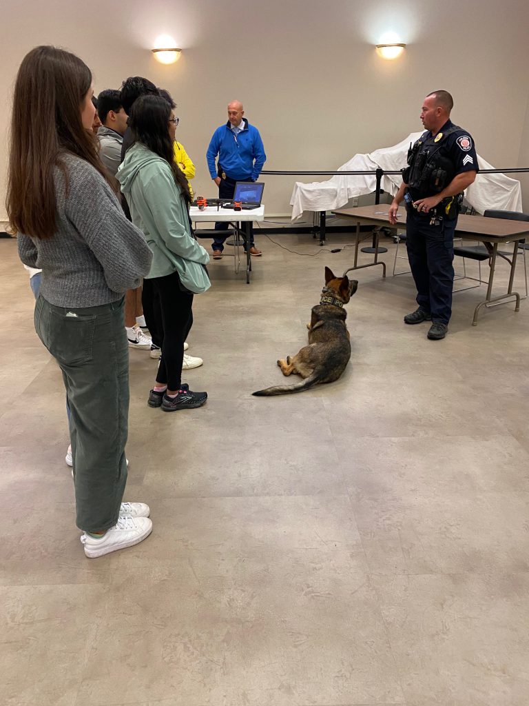 An image of students listening to a police officer who is holding onto a K-9.