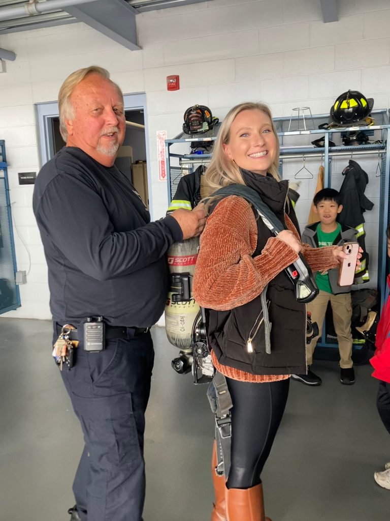 An image of a Boght Hills teacher smiling as she wears a fire fighter's oxygan tank on her back.