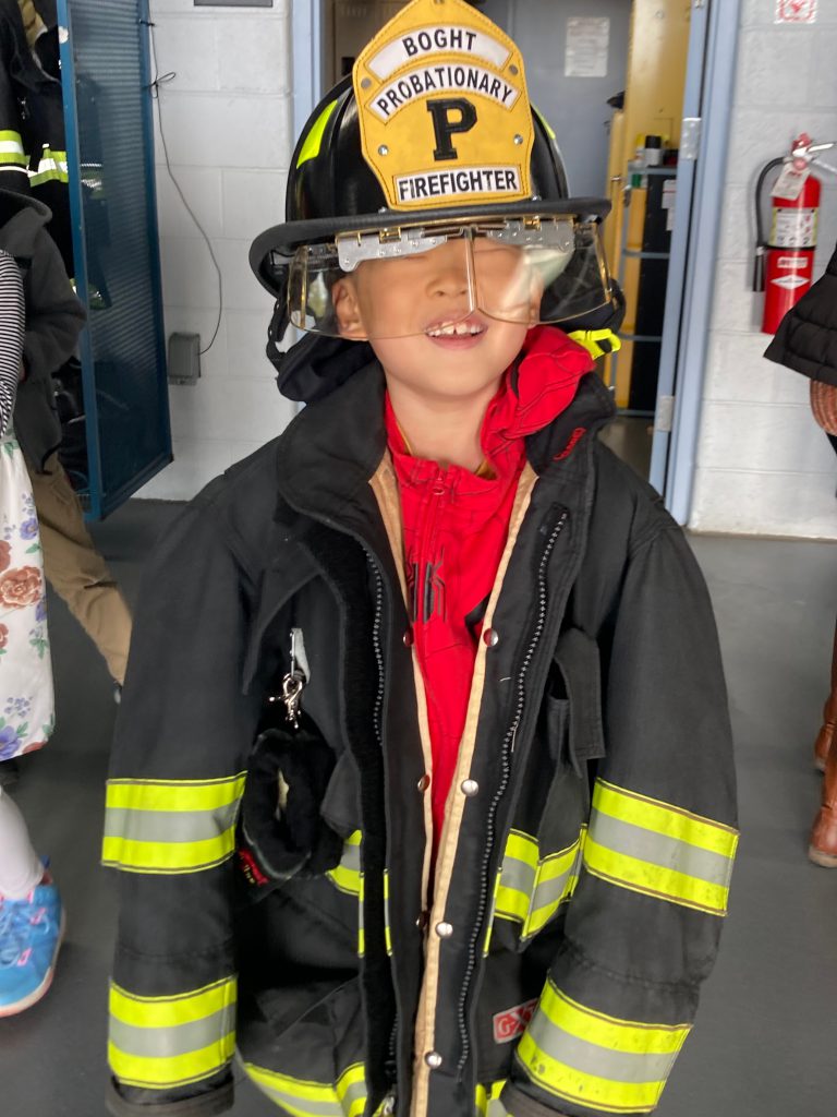 An image of a student smiling while dressed in a fire fighter's helmet and jacket.