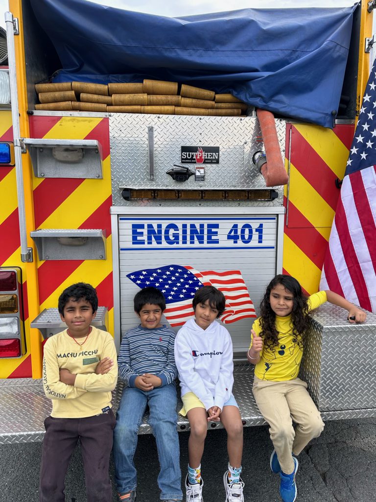 An image of four students sitting on the back of a fire truck.