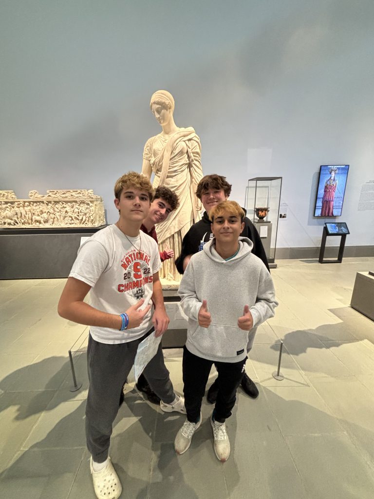 An image of four students giving us the thumbs up in front of a statue.