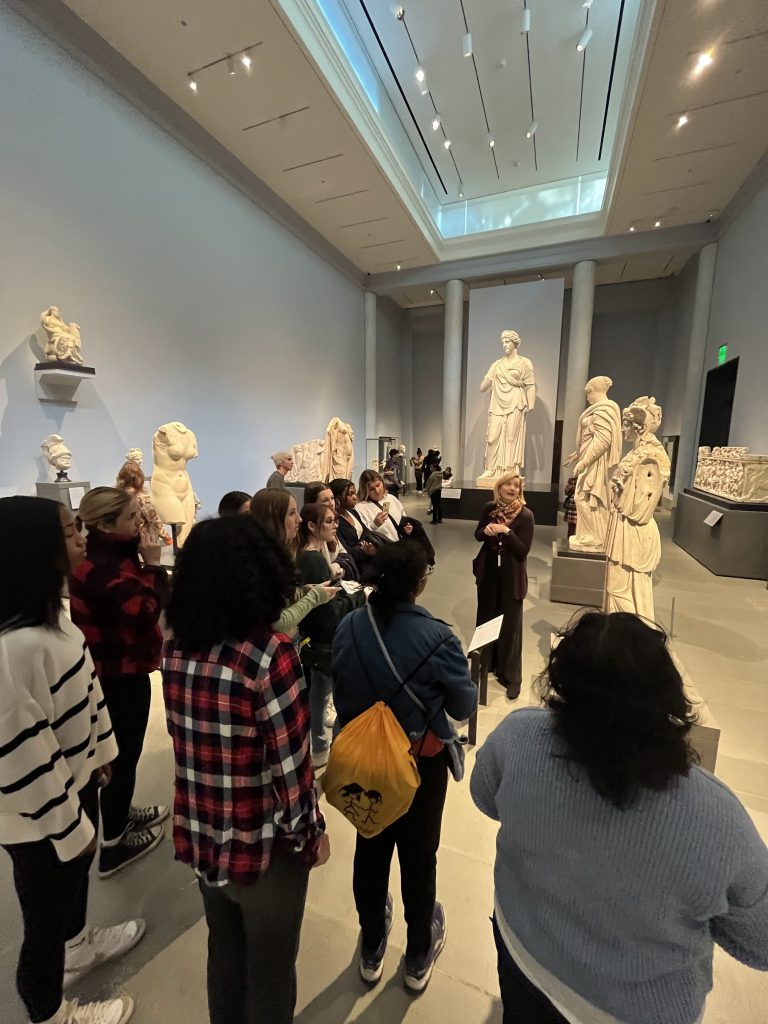 An image of students listening to some speak about the works of art.