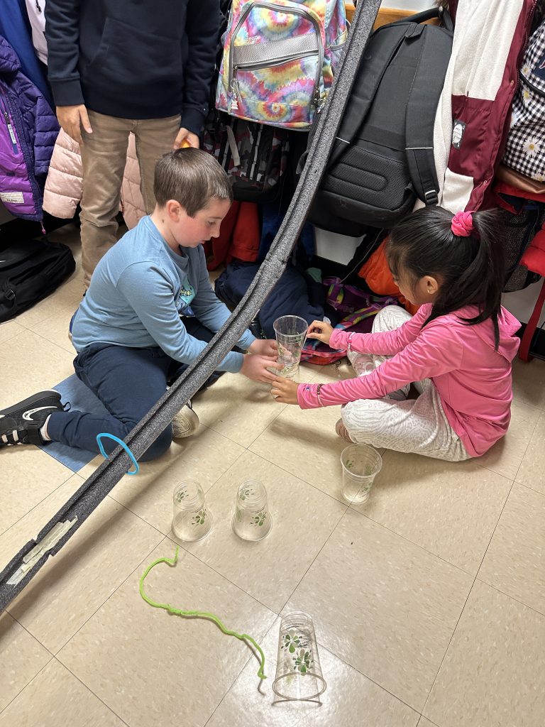 An image of two students using cups to prop up part of their rollercoaster track.