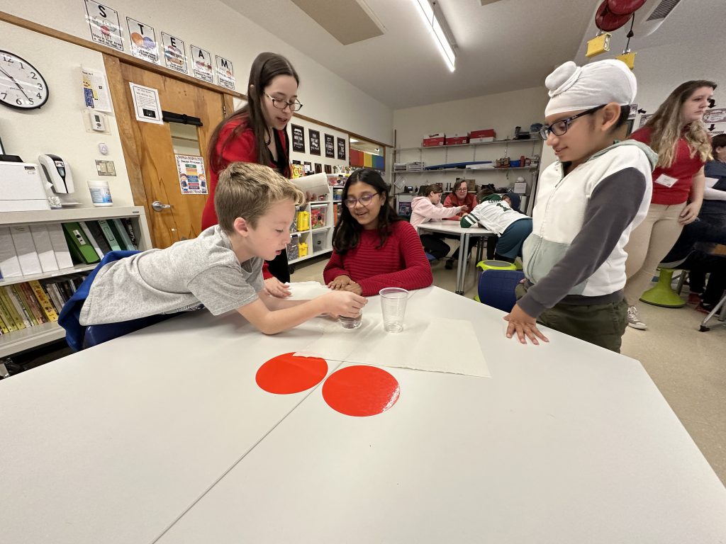 An image of three students working together to separate oil and water with the help of an RPI student.