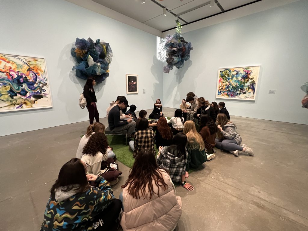An image of students sitting in a room studying various works of art around the room.