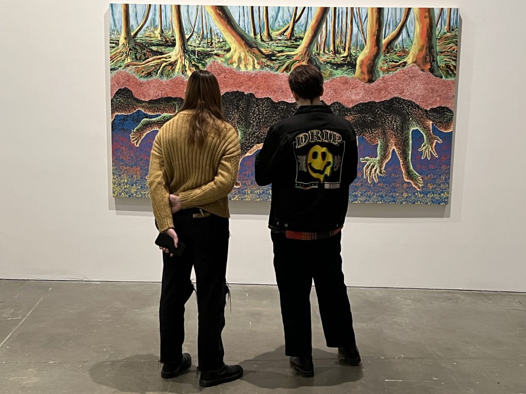 An image of two students studying a piece of art mounted on the wall.