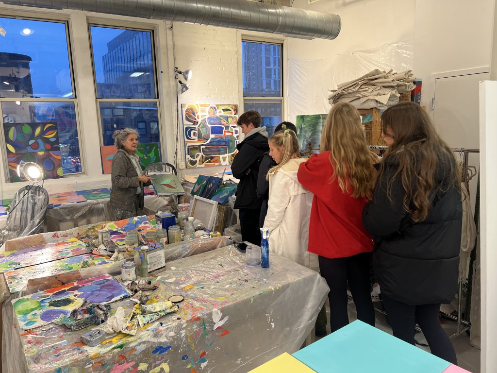 An image of a group of students talking with a practicing artist in studio.