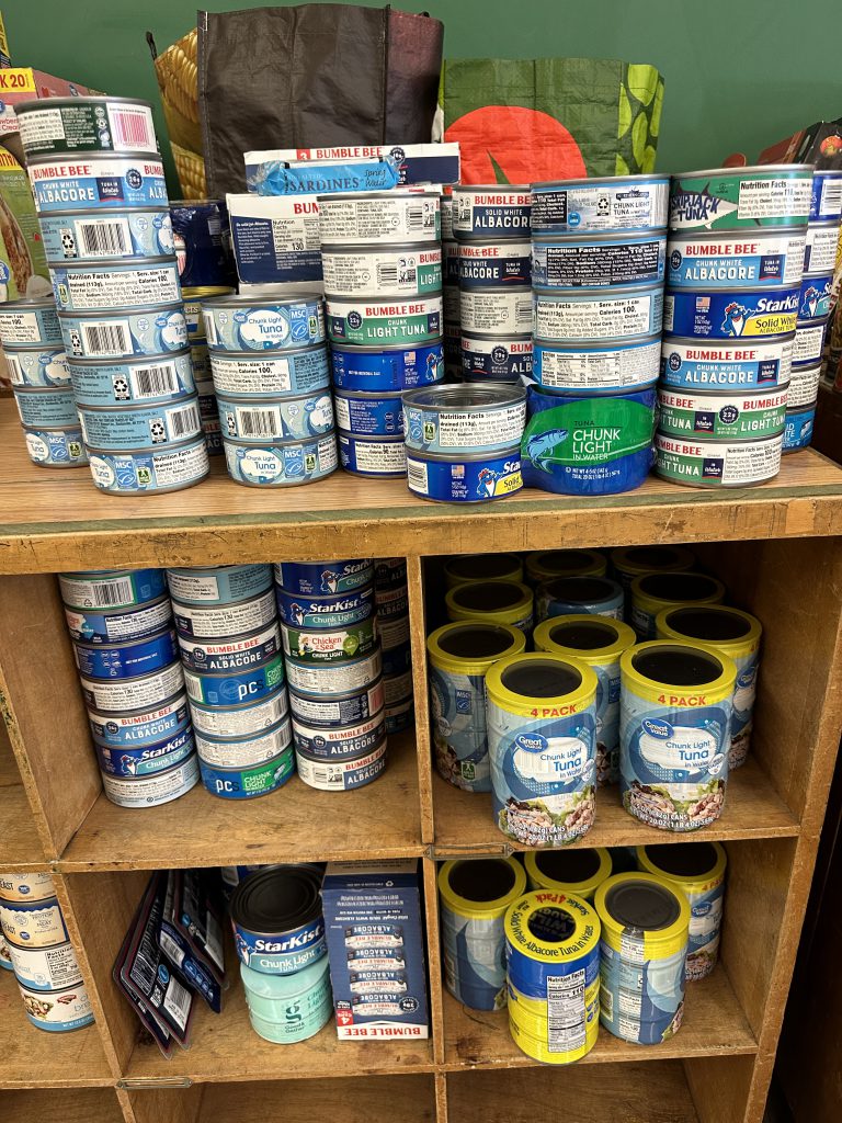 An image of dozens of tuna cans stacked on the shelves of the food pantry.