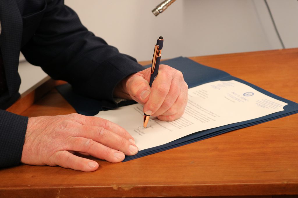An image of Paul Tonko's hand signing a certificate.