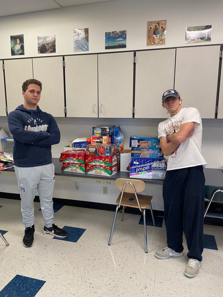 An image of two Shaker students posing with some of the food items gathered for donation.
