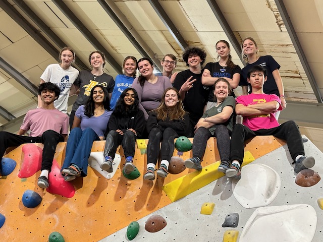 An image of a group of students sitting atop a rock climbing wall.