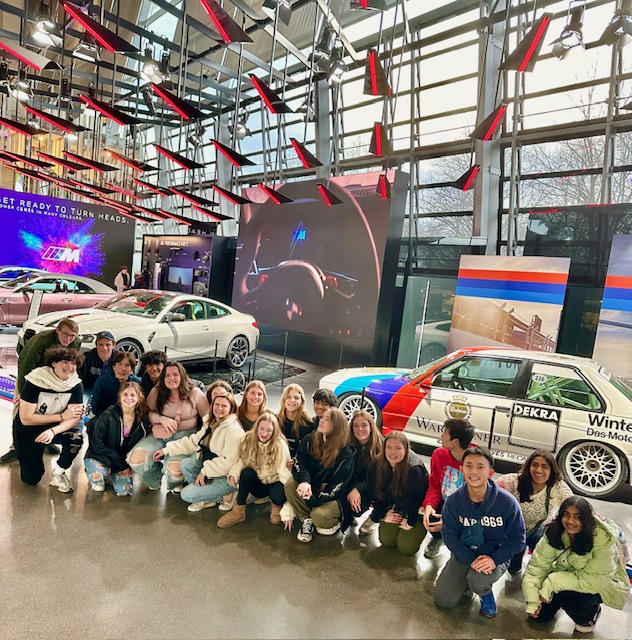 An image of students posing in front of cars.